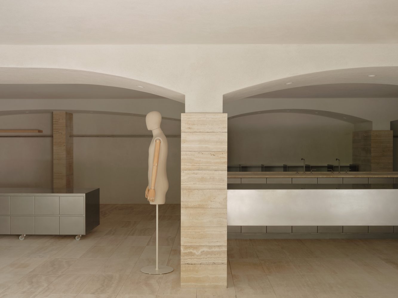 Dress form in a travertine room beneath arches