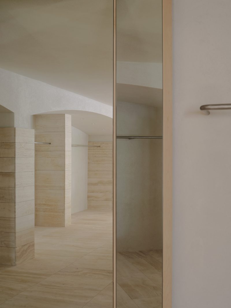 Mirror and steel rail in a pale travertine room